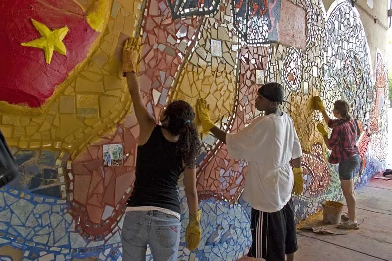 Three people work to install a large outdoor mosaic.