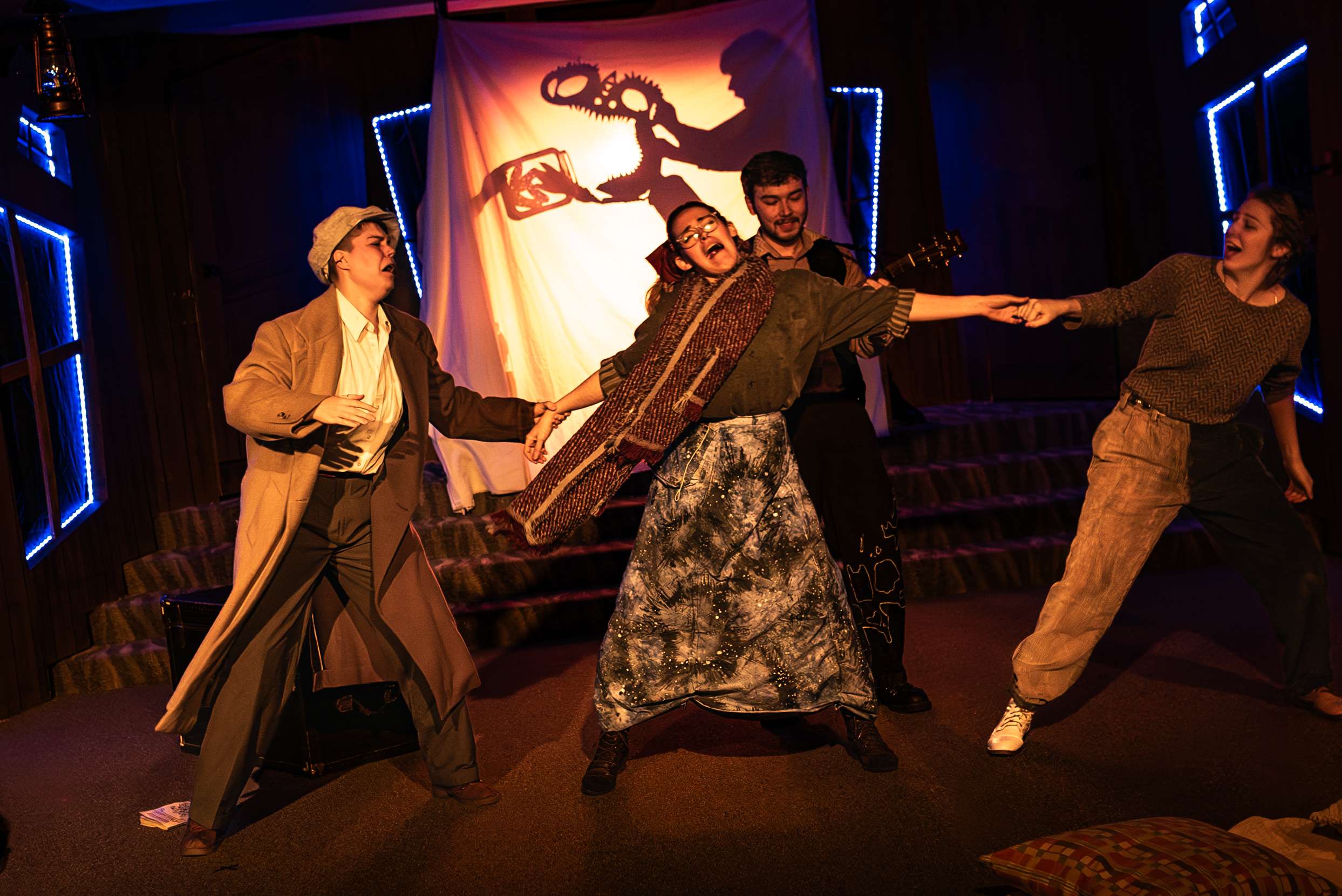 Four actors performing live with three of them holding hands and the fourth behind them