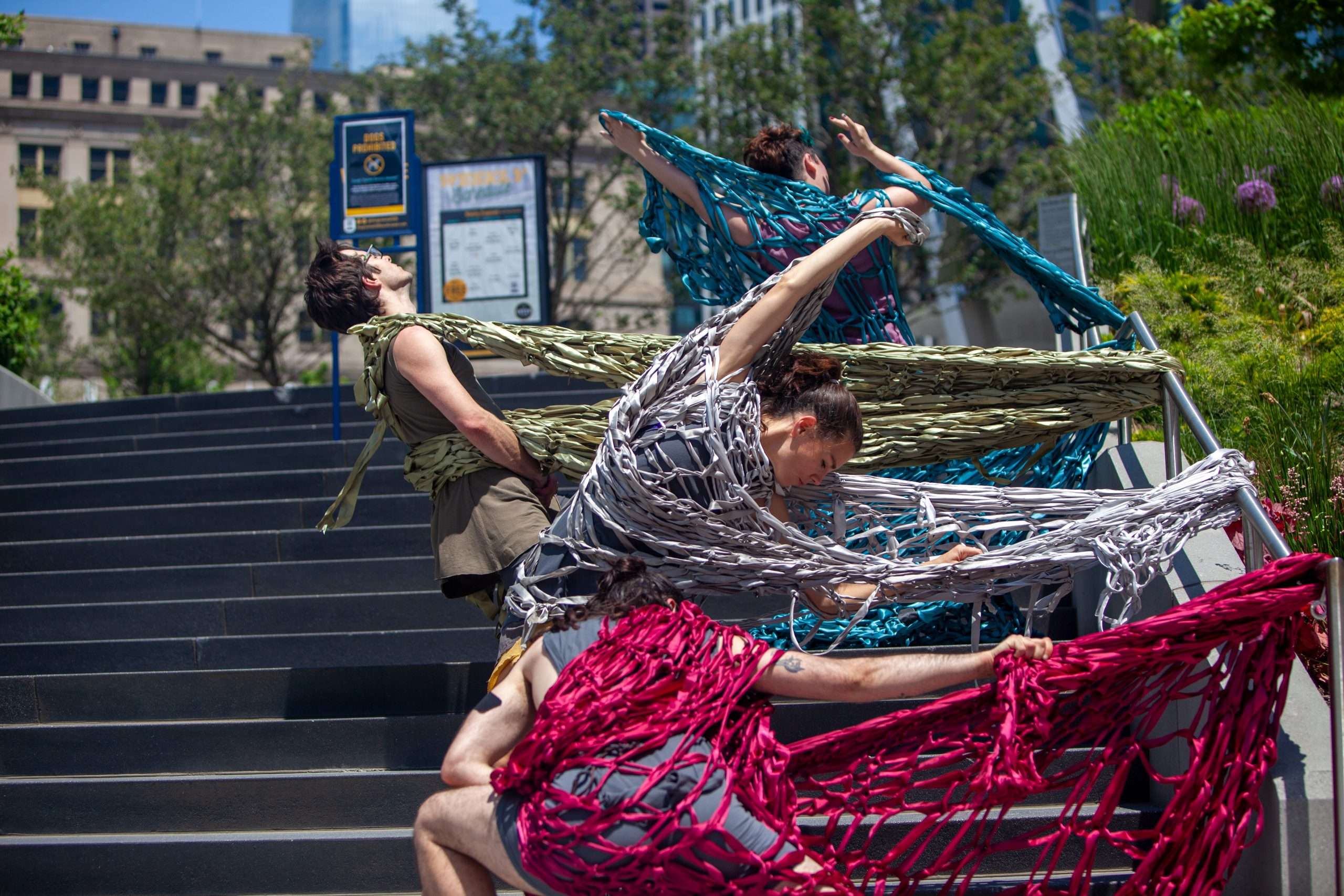 Four dancers performing outside with red, gray, green, and blue nets