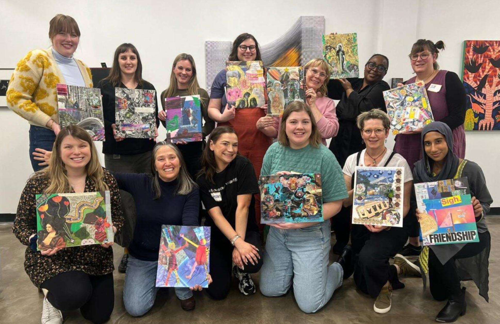 13 women are posing holding their art pieces. Six are in the front row, kneeling. Seven are standing in the back row.
